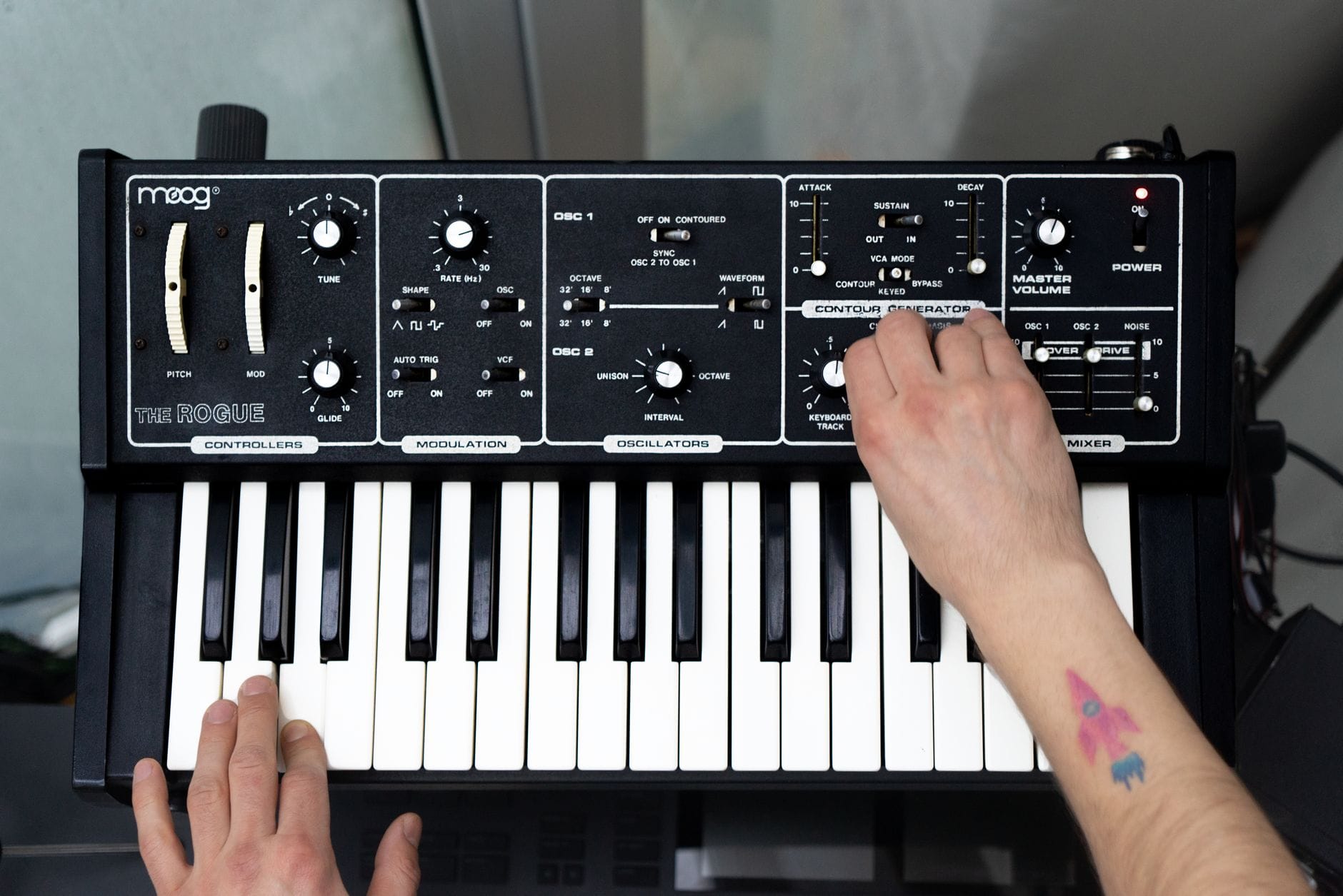 Muzyk gra obiema rękami na syntezatorze Moog, z widocznym panelem sterowania
